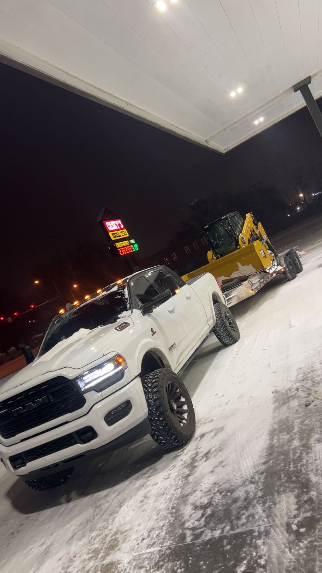 Breedlove pickup truck towing a skid steer on a trailer at night